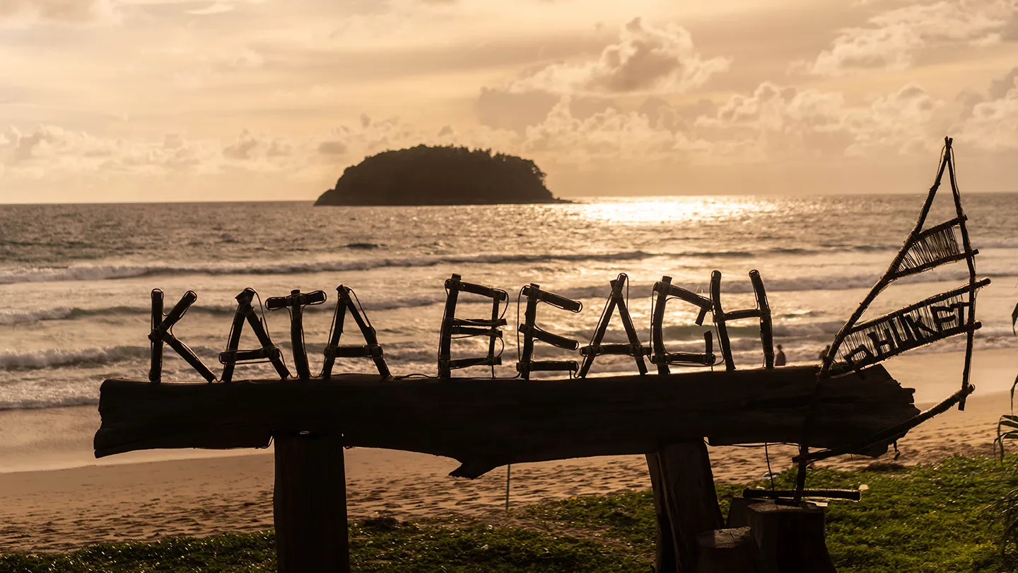 Scenic sunset at Kata Beach with wooden sign and island view in Phuket