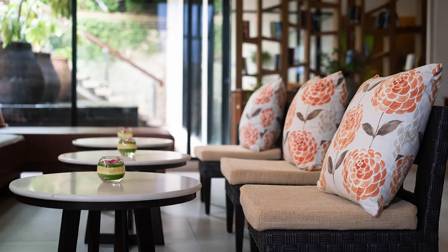 Cosy seating area at Peach Blossom Resort Phuket with floral cushions and small round tables decorated with floating flower bowls in a bright modern lounge setting
